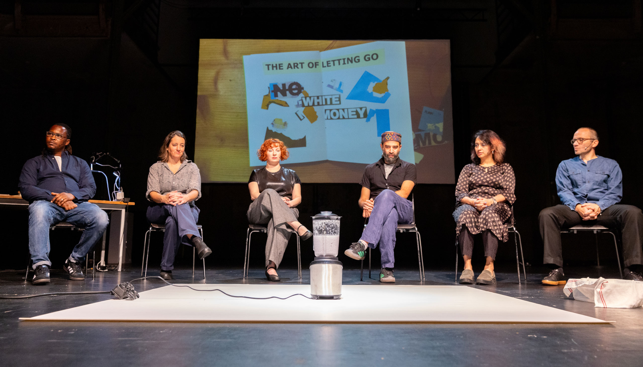 actors sitting in front of a mixer, in the background is a poster that reads "the art of letting go – no more white money"